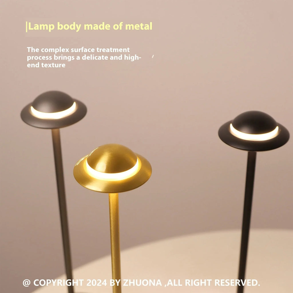 UFO-shaped metal desk lamp with saucer design in grey finish on a wooden table, demonstrating cordless use.