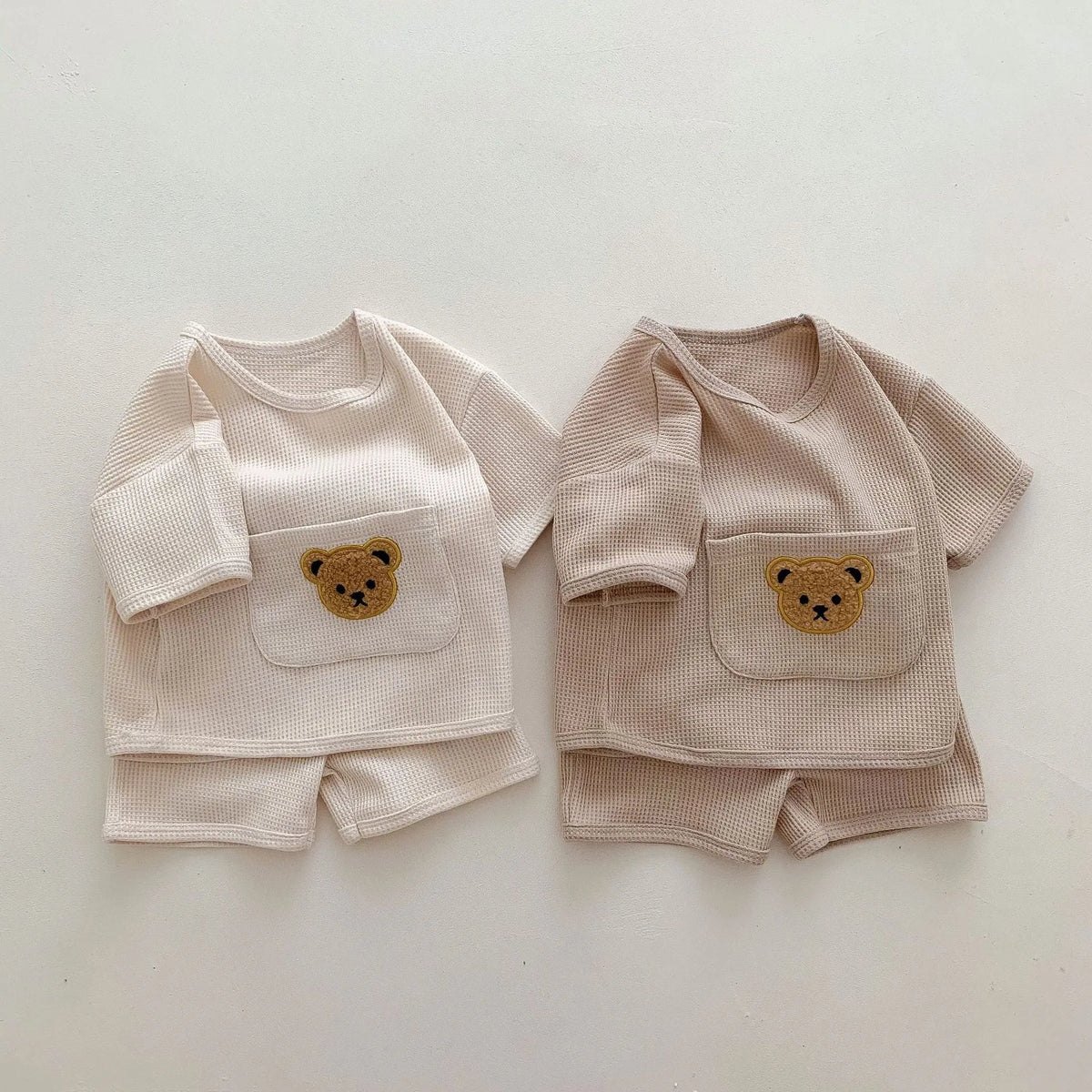 Unisex baby summer suit with bear print cotton top and beige shorts on a neutral background