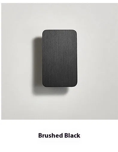 Minimalist black nordic wall lamp mounted beside a bed, emitting warm white light.
