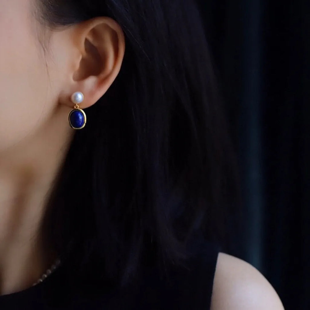 A pair of simple drop earrings featuring a blue lapis lazuli pearl set in patterned sterling silver.