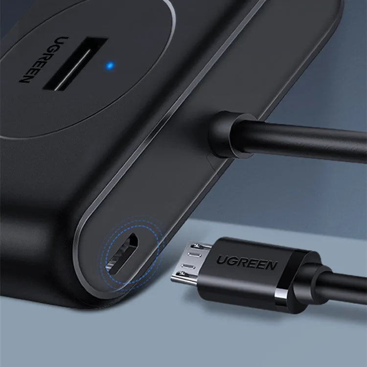 Deep black USB splitter with four ports, Micro USB power port, and indicator light on a desk
