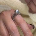 Geometric copper open ring with a black pearl on a model's finger.
