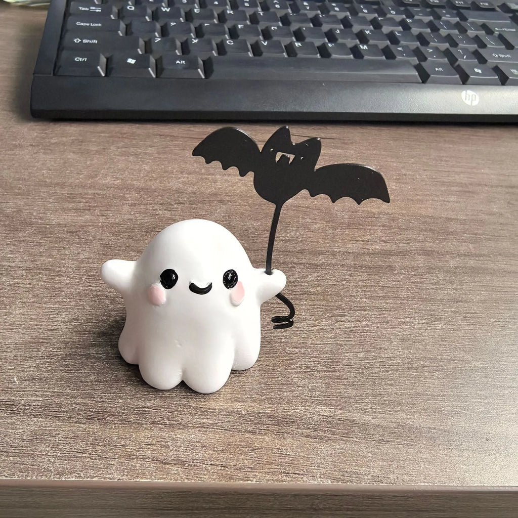 Small white ghost walking a dog and holding a bat, resin Halloween statue on a wooden surface.