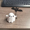 Small white ghost walking a dog and holding a bat, resin Halloween statue on a wooden surface.