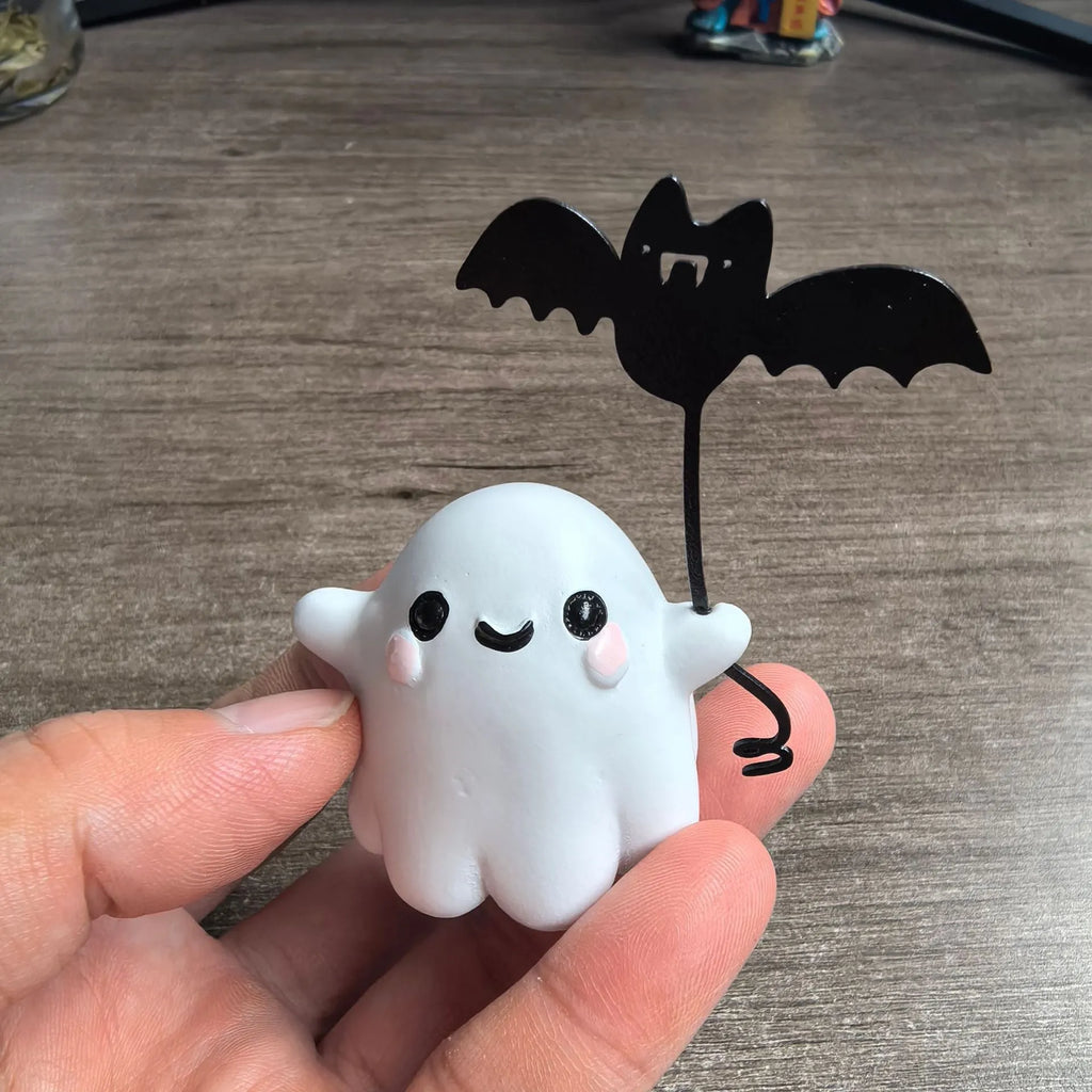 Small white ghost walking a dog and holding a bat, resin Halloween statue on a wooden surface.