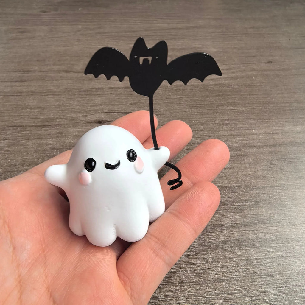 Small white ghost walking a dog and holding a bat, resin Halloween statue on a wooden surface.