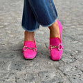 Green suede flat-heel loafers with a round toe and metal buckle fastening on a white background.