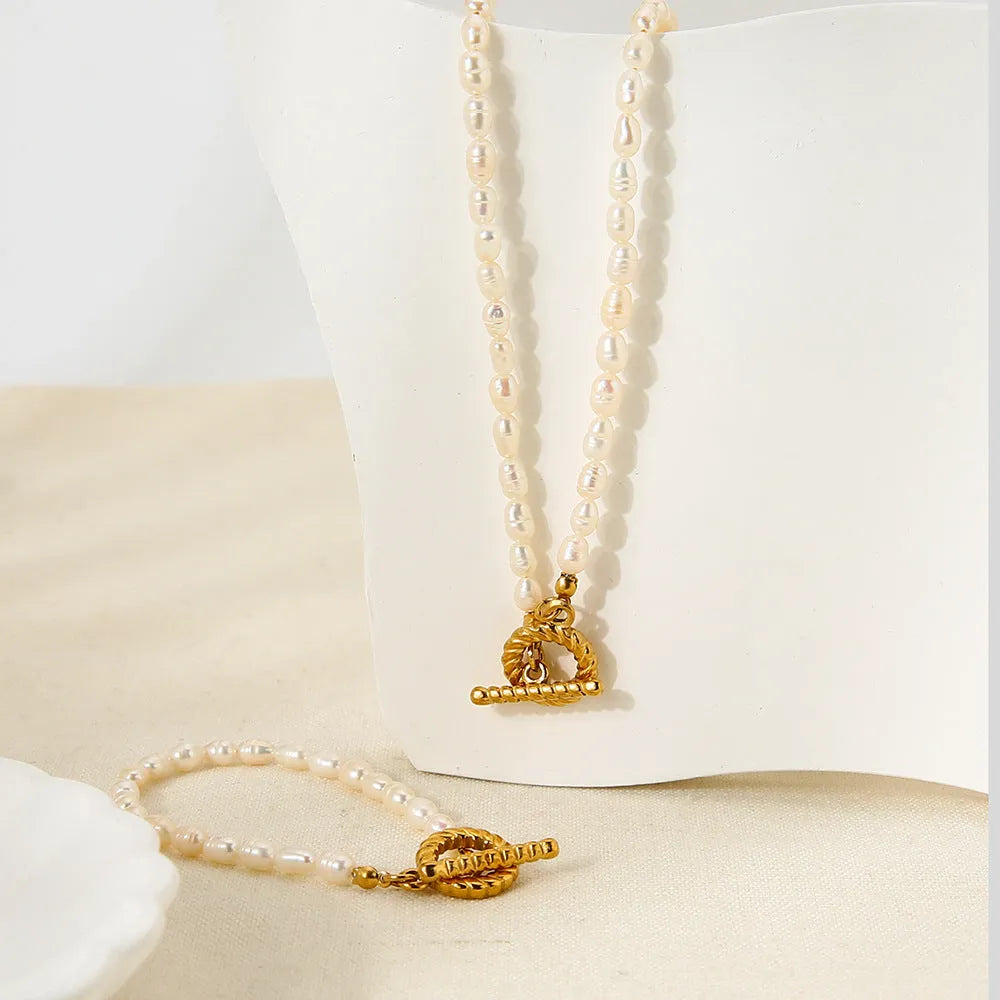 Women's freshwater pearl and geometric stainless steel necklace and bracelet set on a grey background