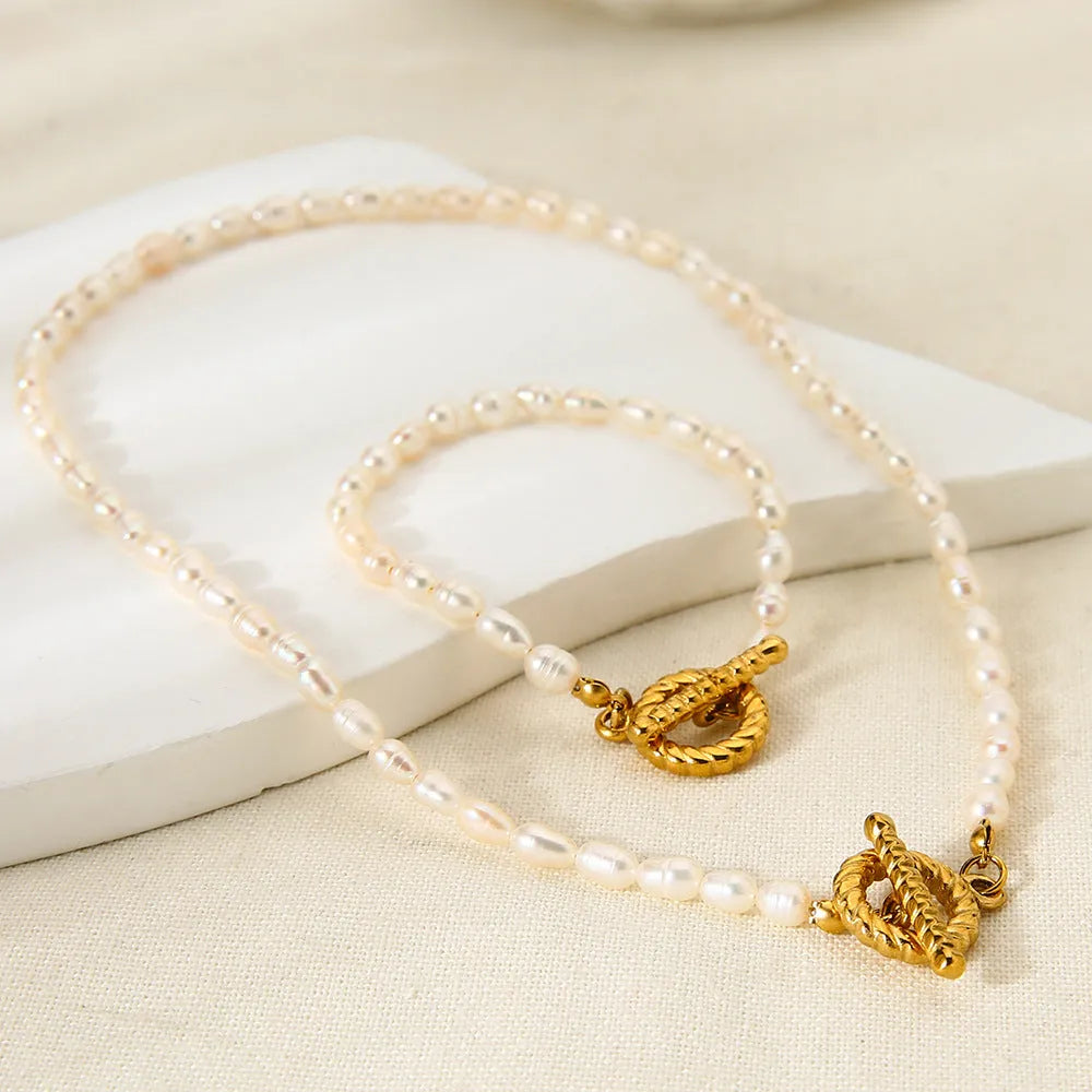 Women's freshwater pearl and geometric stainless steel necklace and bracelet set on a grey background