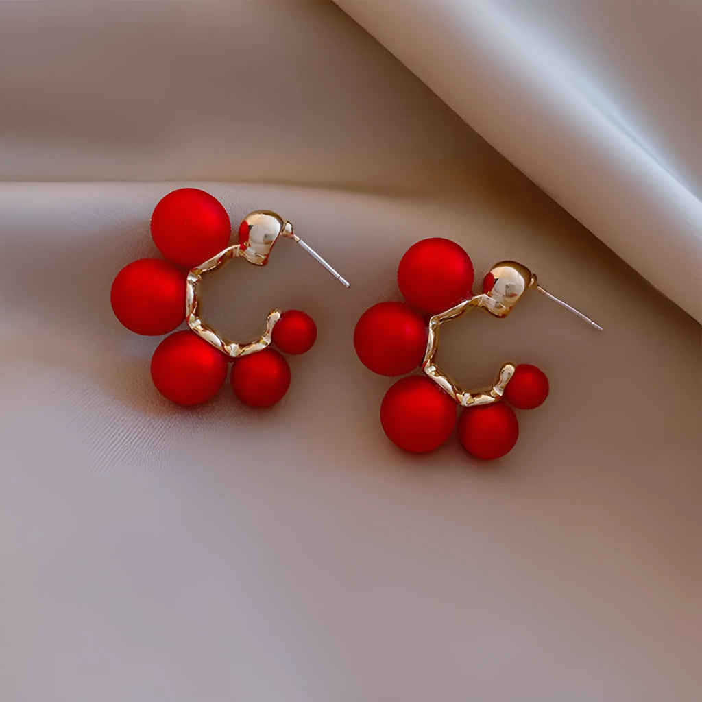 A pair of red bell-shaped alloy earrings for women next to a pair of plain white alloy earrings.