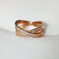 A silver or rose gold plated metal ring with a cross design and small zircon stones, shown on a finger.
