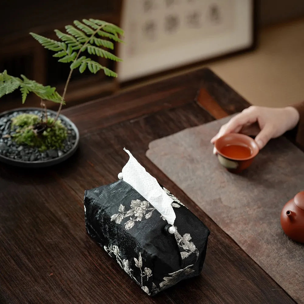 White Chinese brocade tissue box with embroidered plum blossoms on a side table.