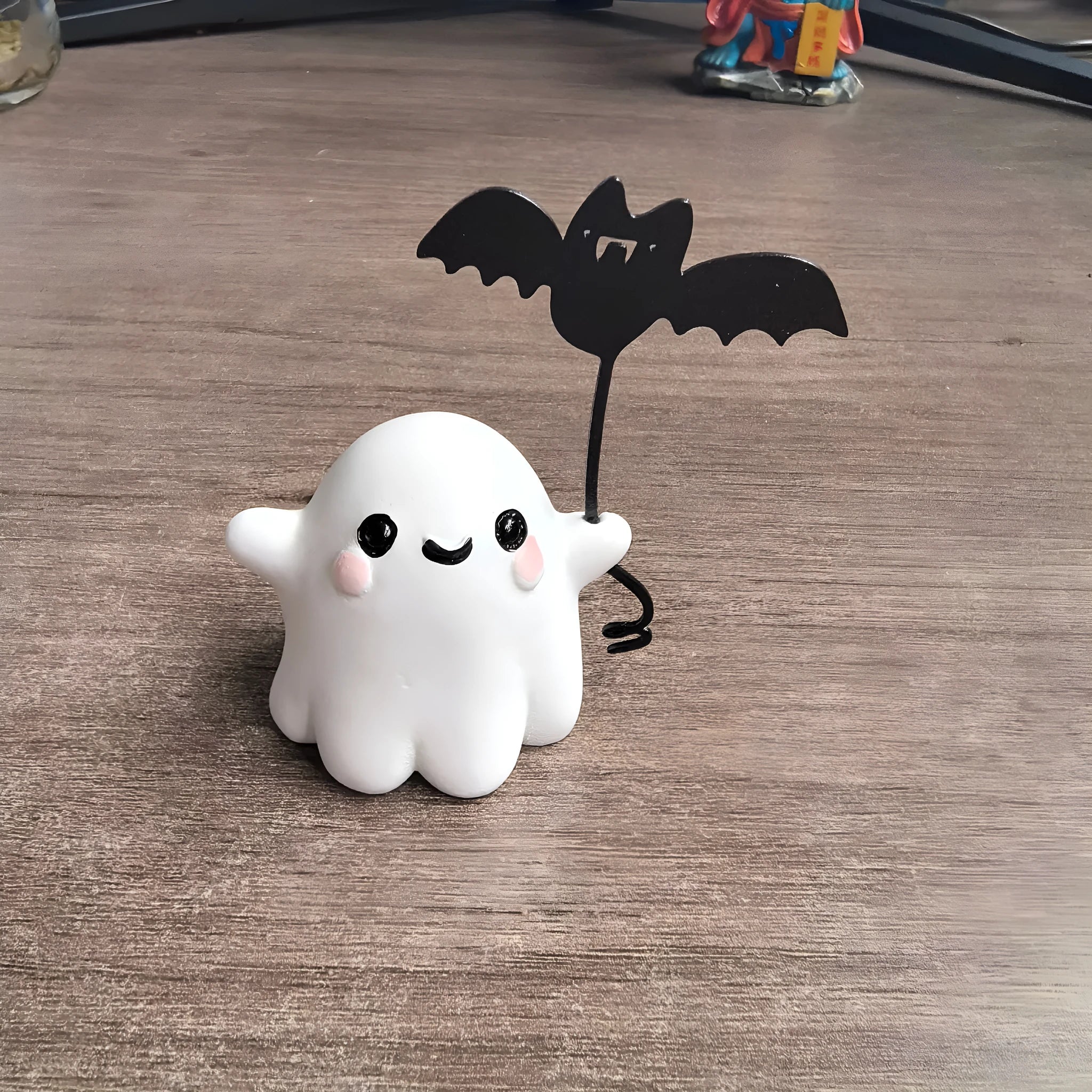 Small white ghost walking a dog and holding a bat, resin Halloween statue on a wooden surface.