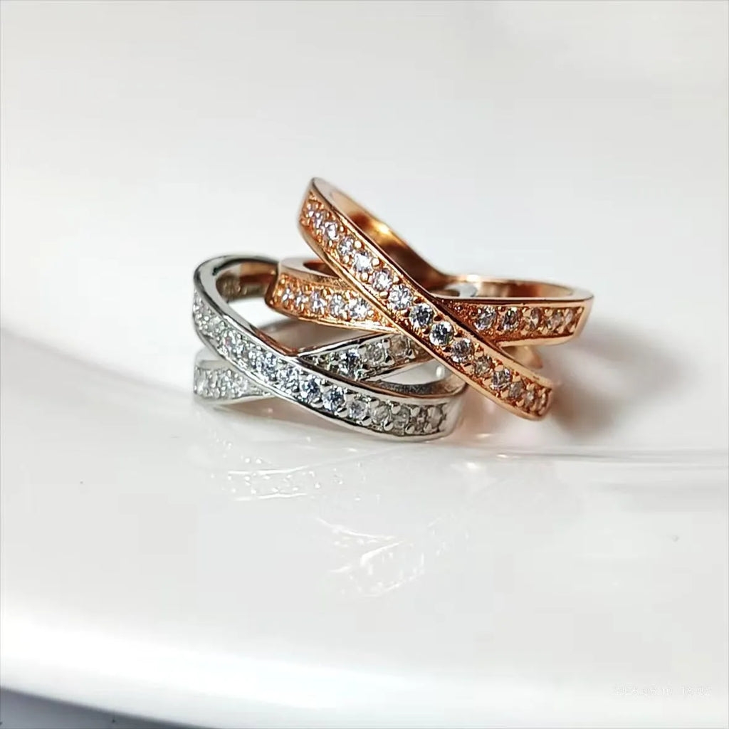 A silver or rose gold plated metal ring with a cross design and small zircon stones, shown on a finger.