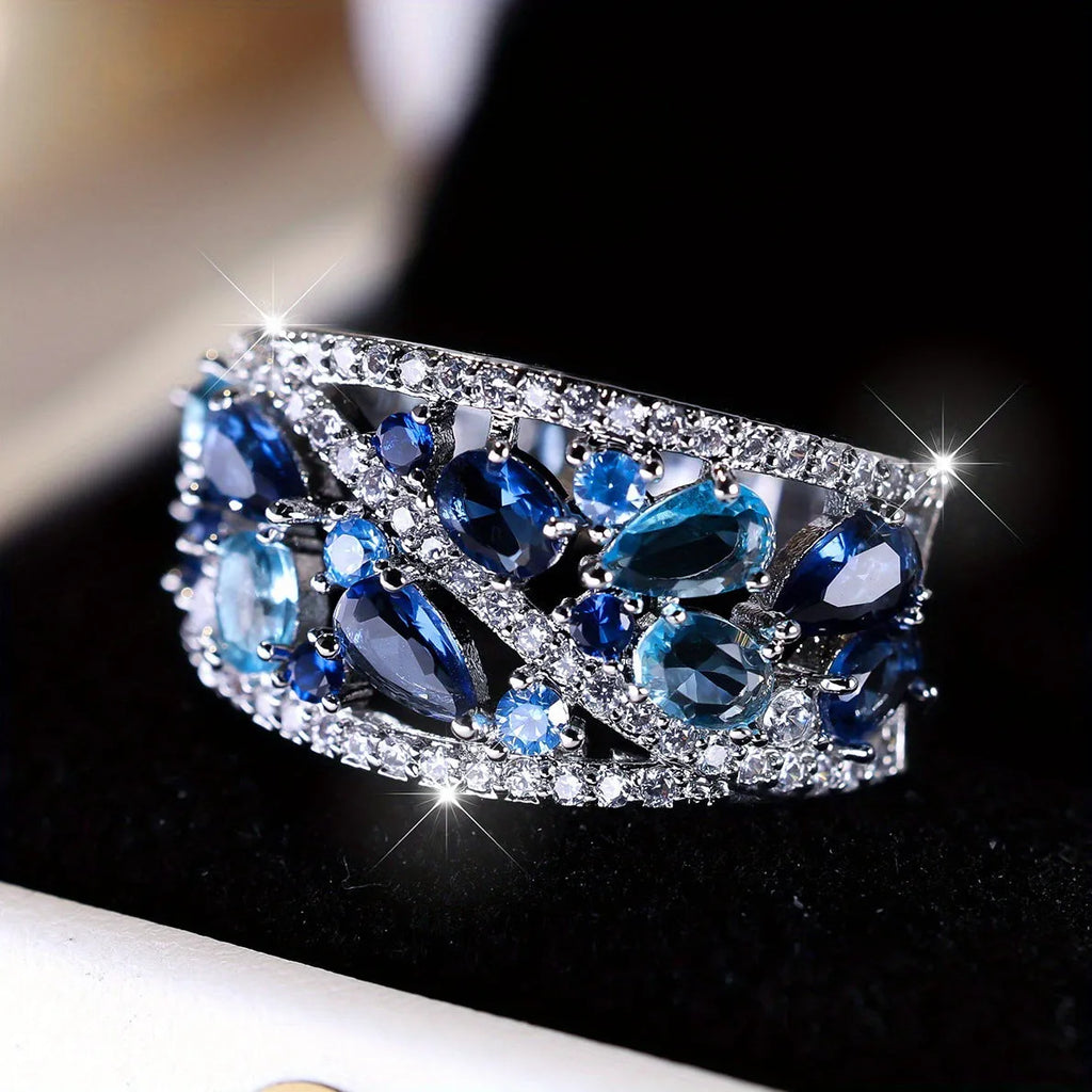 Women's hollow round fashion ring in gold and platinum finishes with blue and white stone accents.