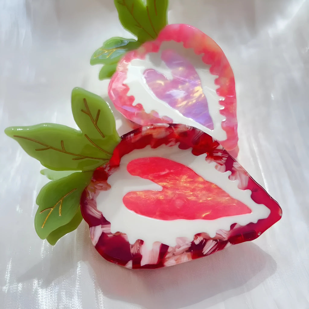 A close-up of a handmade strawberry-shaped hairpin in either red or pink colour on a light background.