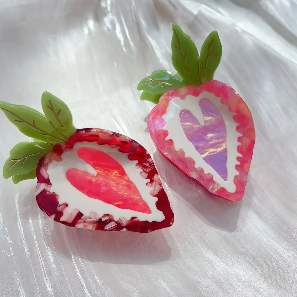 A close-up of a handmade strawberry-shaped hairpin in either red or pink colour on a light background.
