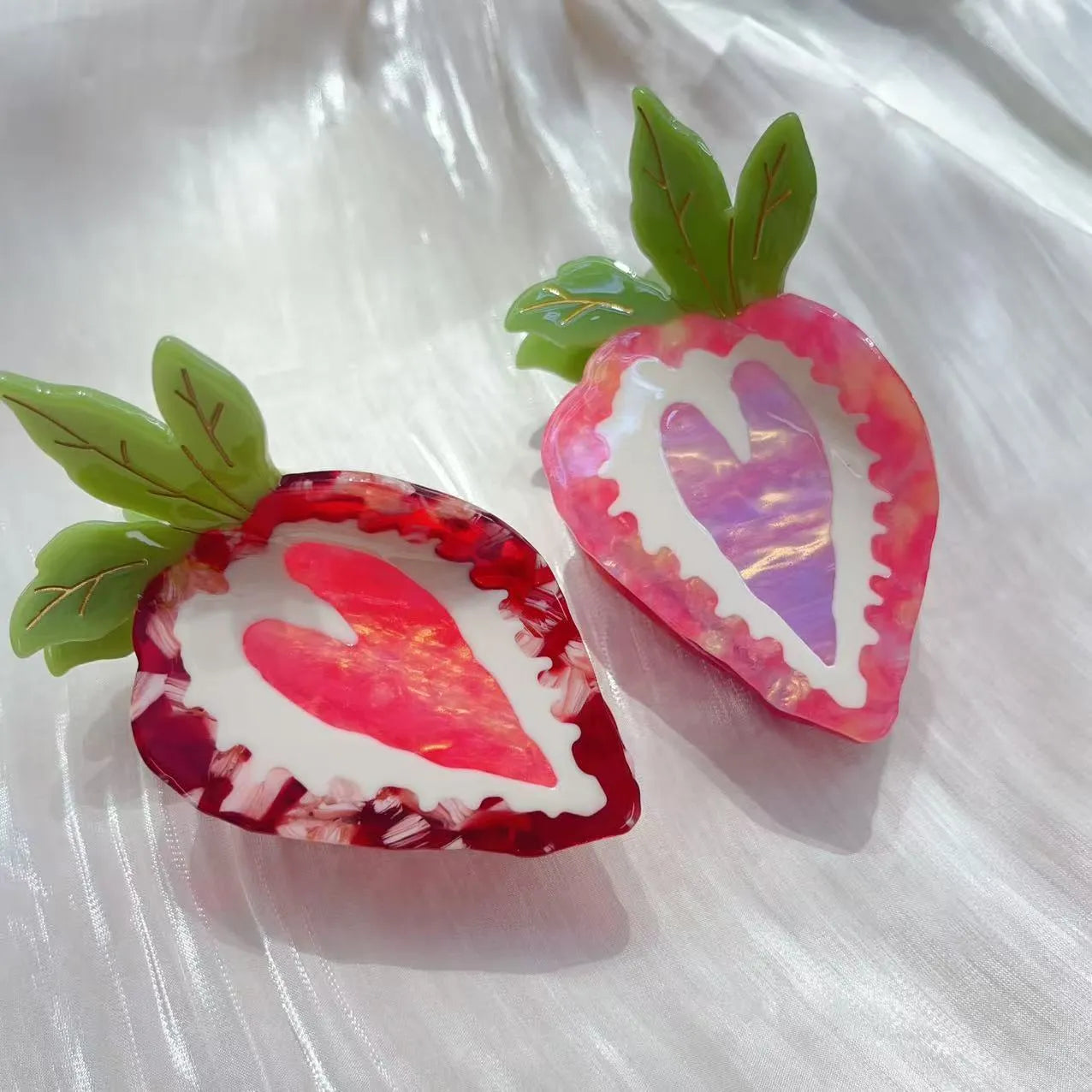 A close-up of a handmade strawberry-shaped hairpin in either red or pink colour on a light background.