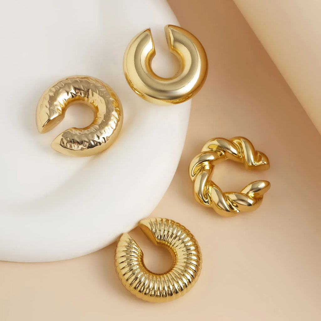 Set of four geometric gold and silver tone clip-on earrings for women on a flat lay.
