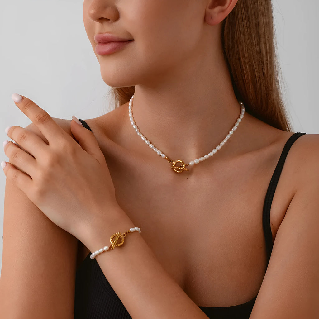 Women's freshwater pearl and geometric stainless steel necklace and bracelet set on a grey background