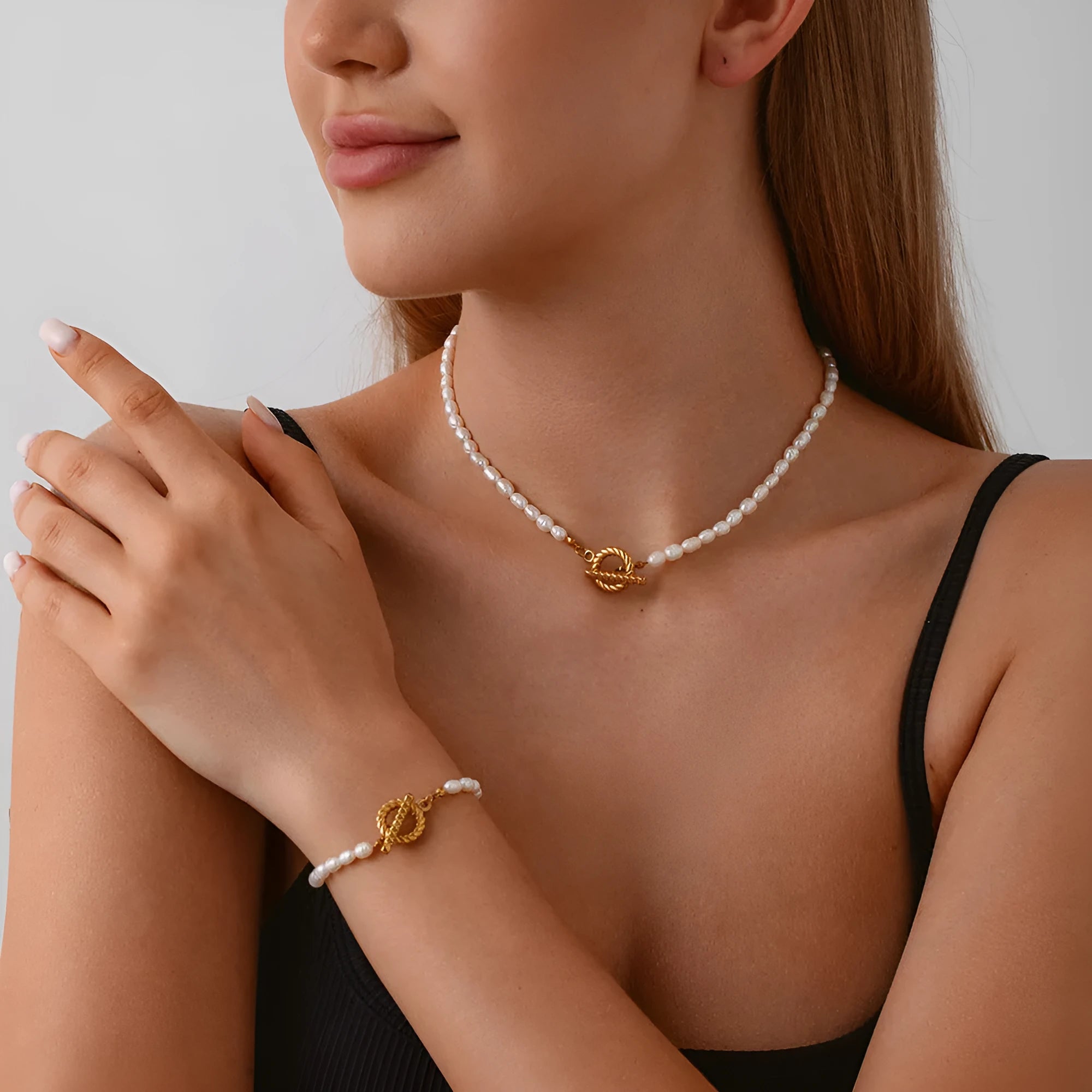 Women's freshwater pearl and geometric stainless steel necklace and bracelet set on a grey background