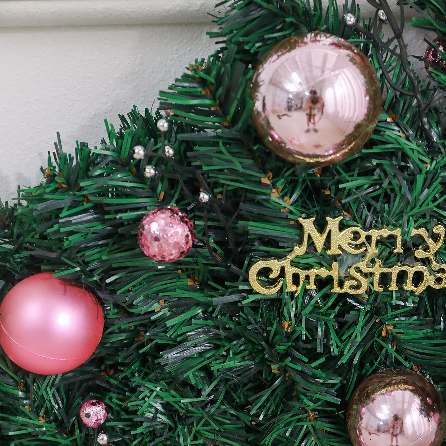 Long pink Christmas rattan garland with small decorative fruits and warm white LED lights draped on a mantelpiece.