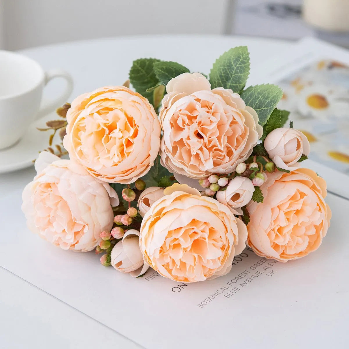 Artificial silk peony bouquet in a vase with champagne coloured blooms and green leaves