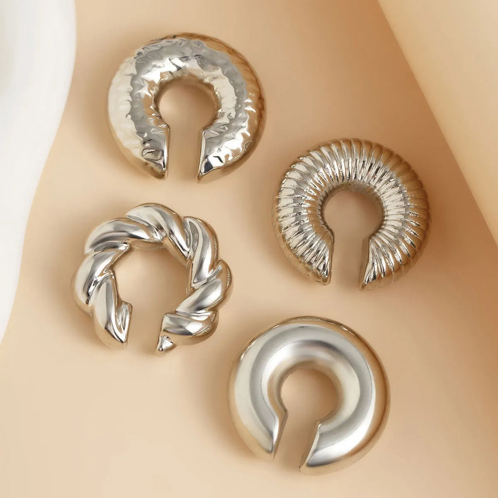 Set of four geometric gold and silver tone clip-on earrings for women on a flat lay.
