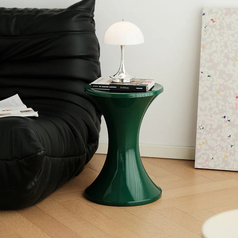 Green plastic hourglass-shaped shoe changing stool on a wooden floor.