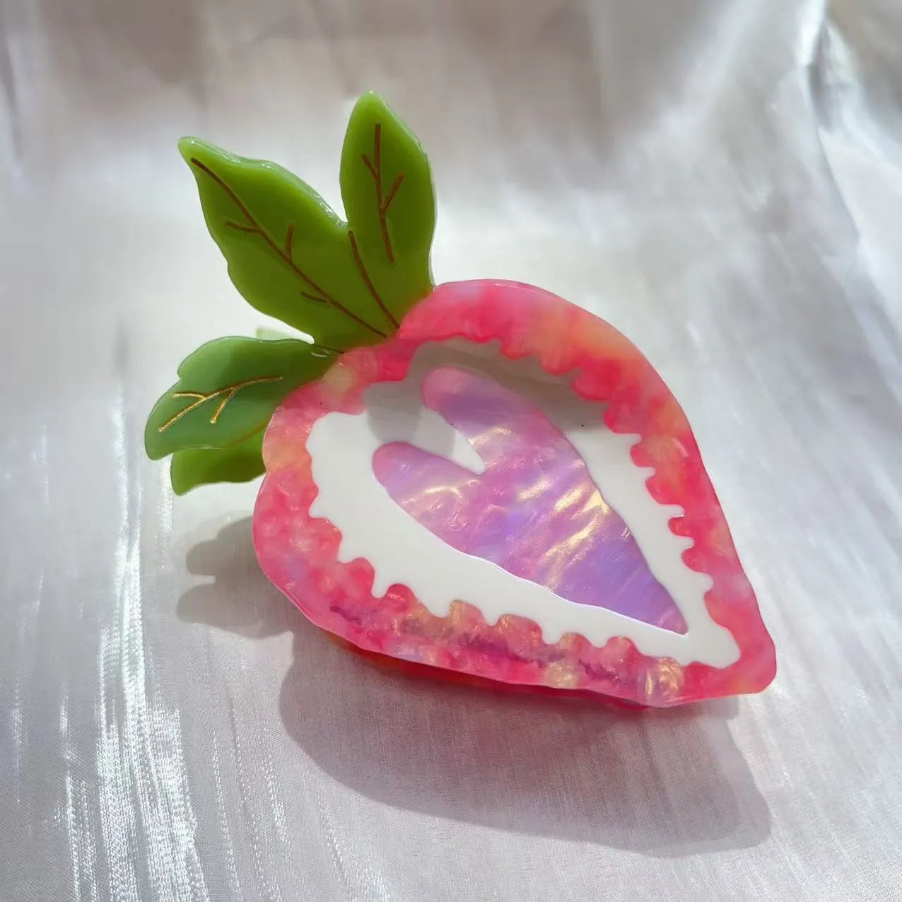 A close-up of a handmade strawberry-shaped hairpin in either red or pink colour on a light background.