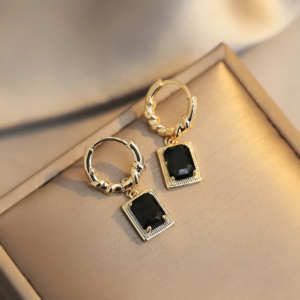 A pair of black geometric quadrilateral stud earrings with zircon stones on a copper setting.