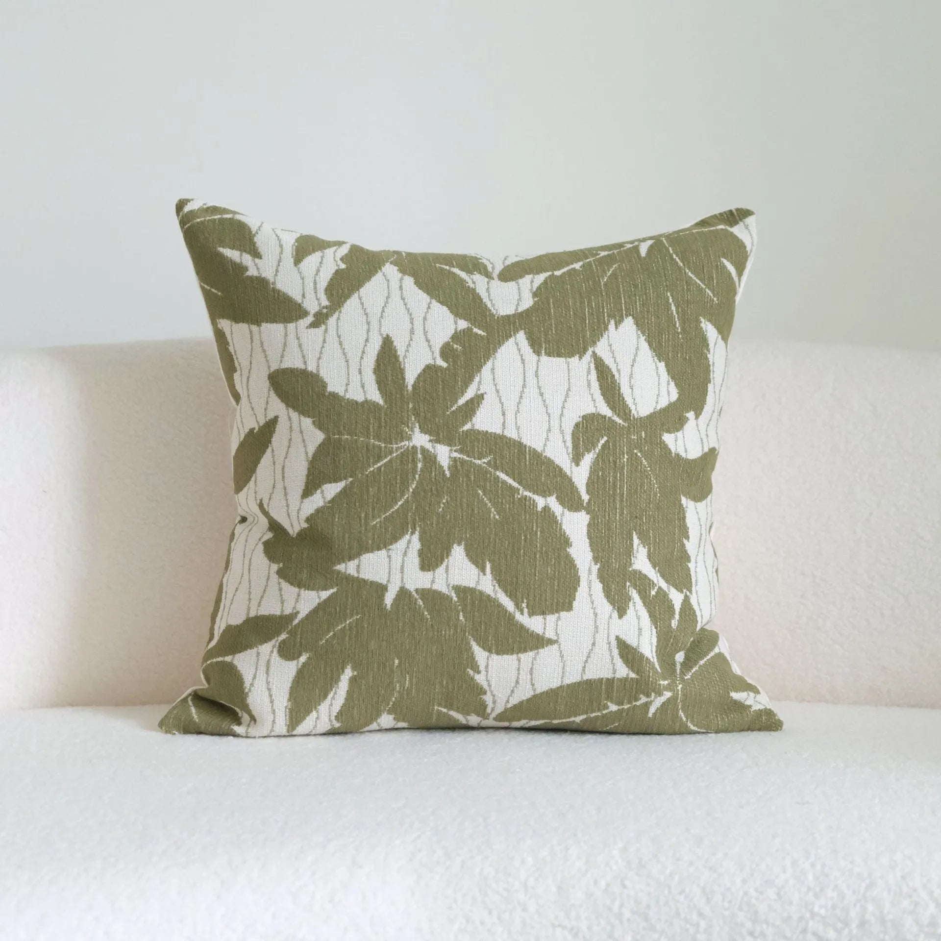 Green cotton and linen hotel sample pillow with botanical pattern and tassel detail on a display bed.