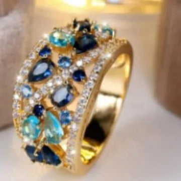 Women's hollow round fashion ring in gold and platinum finishes with blue and white stone accents.