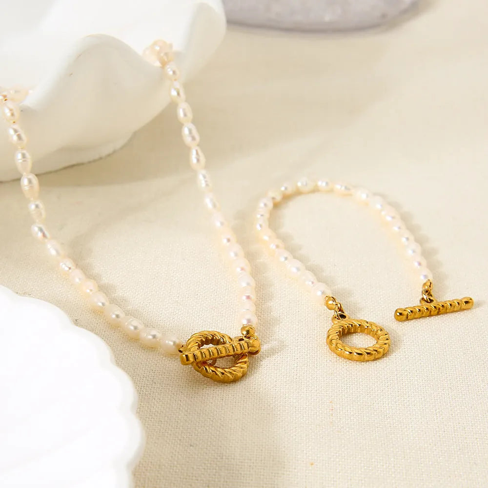 Women's freshwater pearl and geometric stainless steel necklace and bracelet set on a grey background