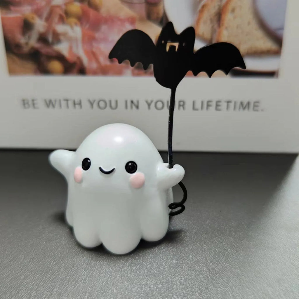 Small white ghost walking a dog and holding a bat, resin Halloween statue on a wooden surface.