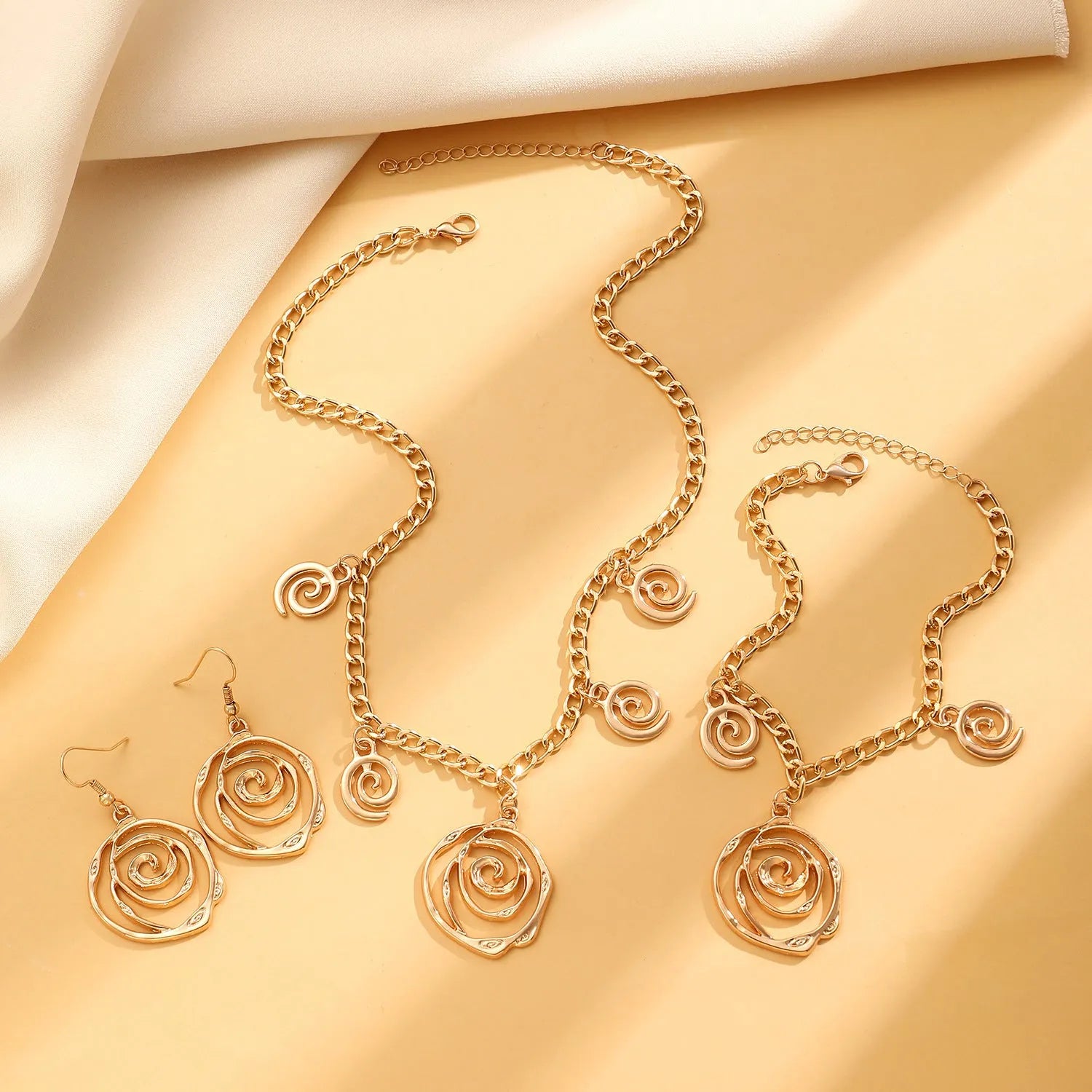 Spiral donut design jewellery set showing necklace, bracelet and ear hooks in gold finish
