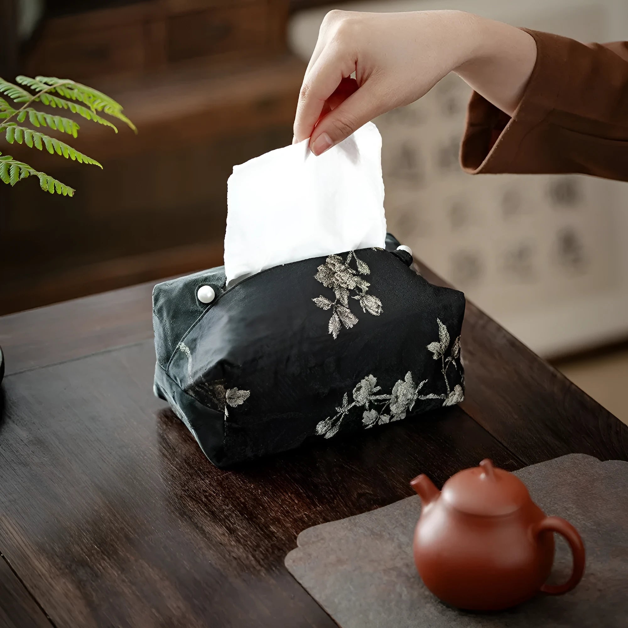 White Chinese brocade tissue box with embroidered plum blossoms on a side table.