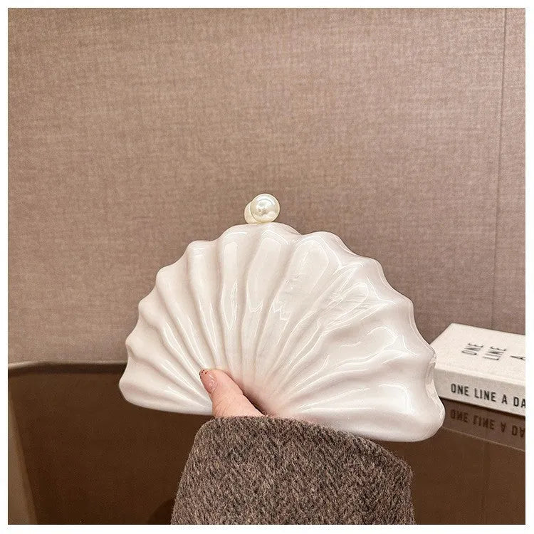 Acrylic shell-shaped clutch bag in champagne with silver chain on white background