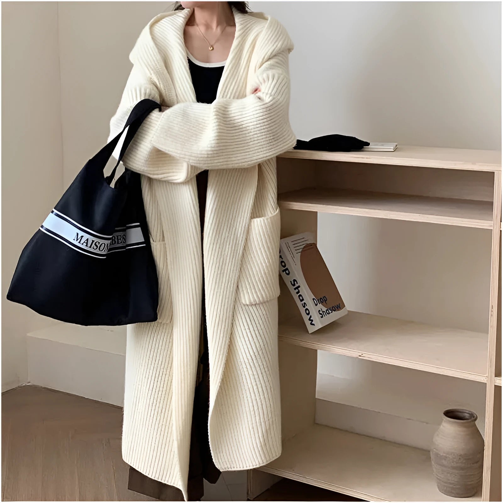 A woman wearing a long, loose, hooded cardigan coat in a neutral colour, showing its oversized fit and length.