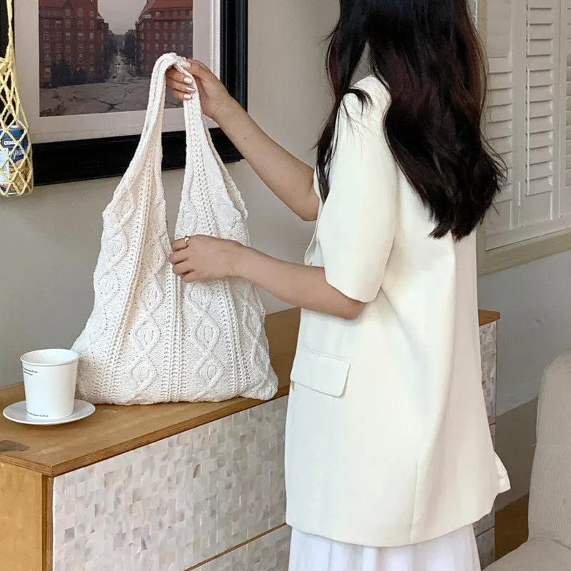Women's white hollow knitted crochet tote bag with double shoulder straps, shown on a table.