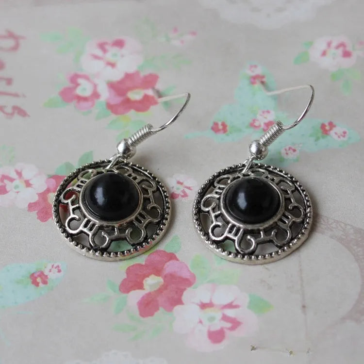 A pair of handmade ethnic earrings with a silver flower disc design, turquoise stones, and red decorative accents.