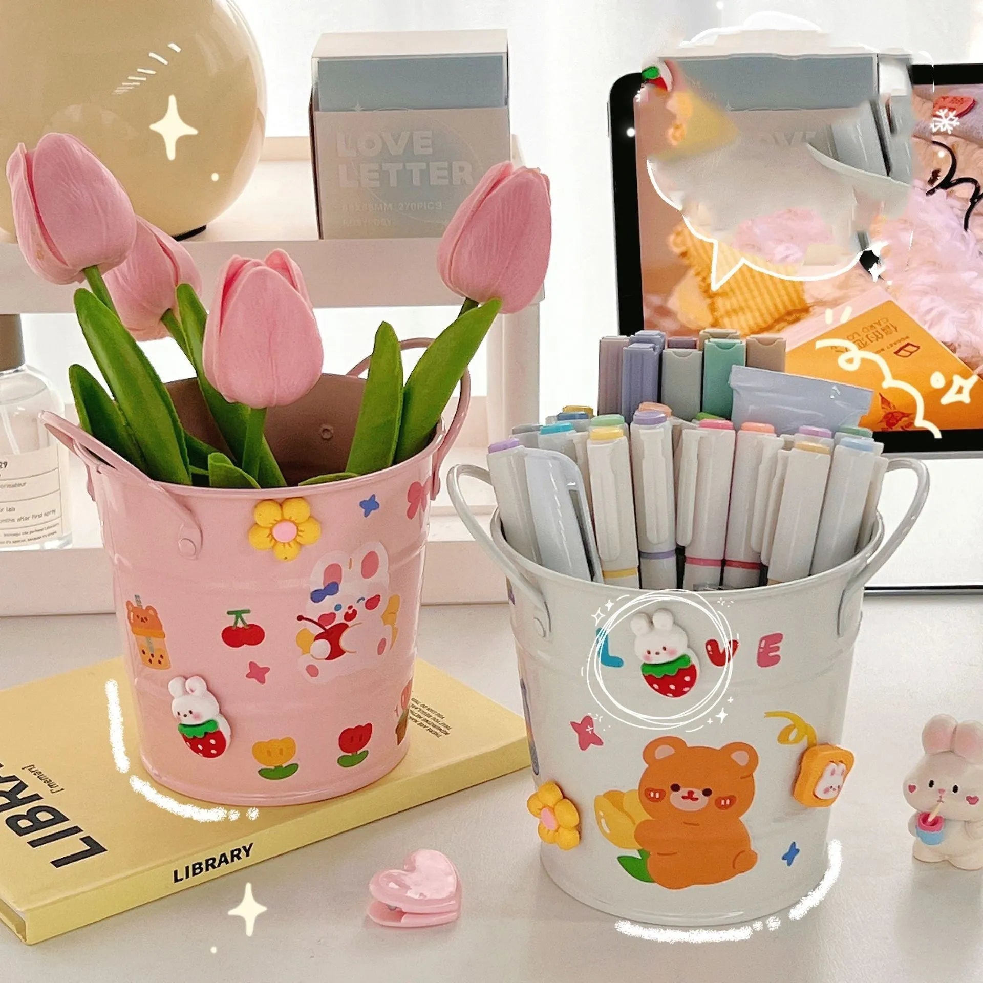 Round metal pen holder in a choice of colours, some with decorative sticker patches, on a wooden desk.