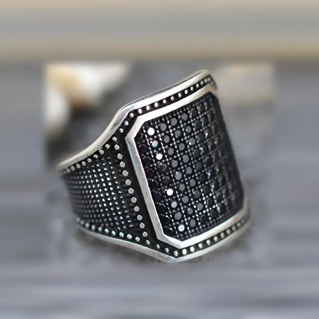 Black alloy ring with copper inlay details and a central sparkling zircon stone on a plain background.