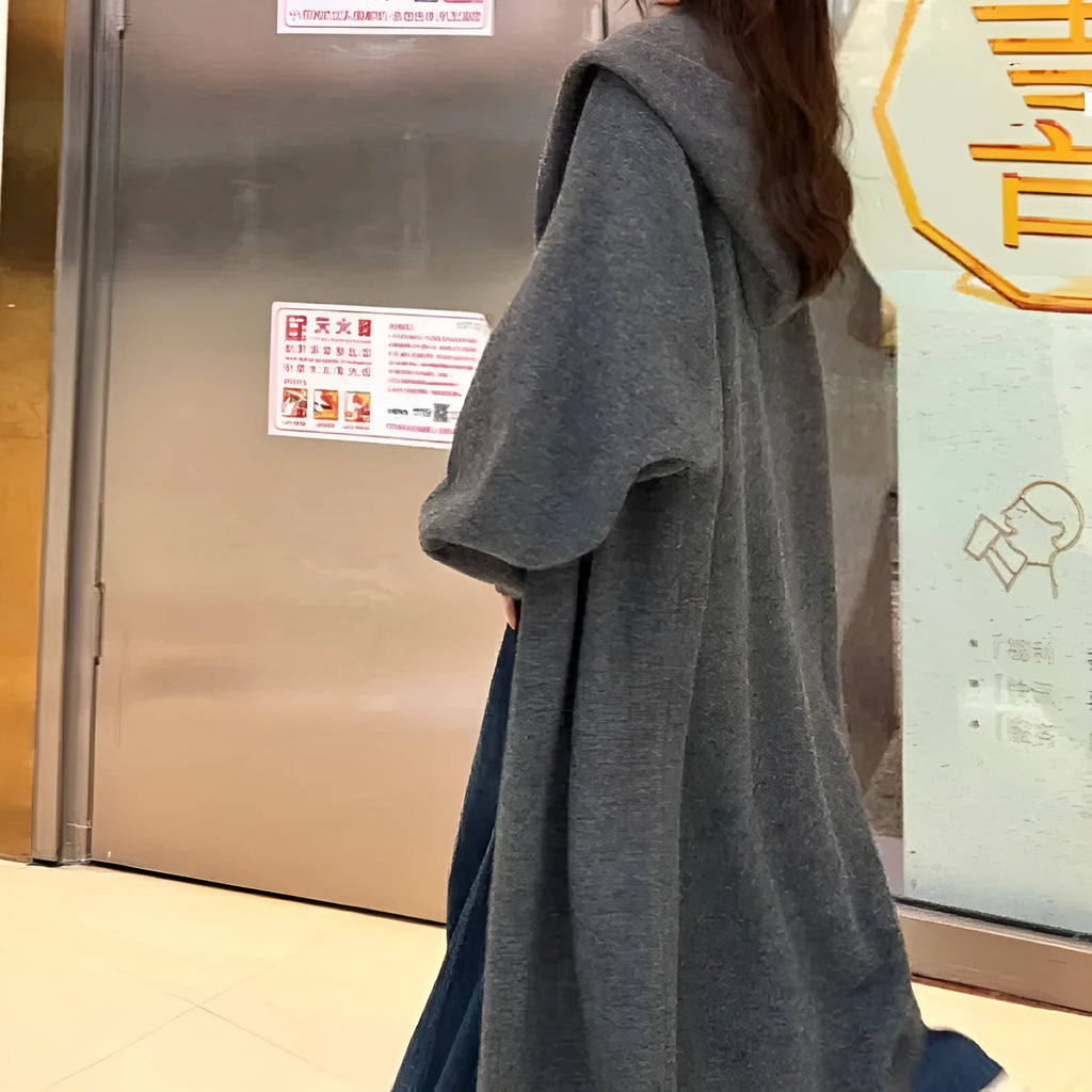 A woman wearing a long, loose, beige hooded knitted cardigan in a Korean casual style.