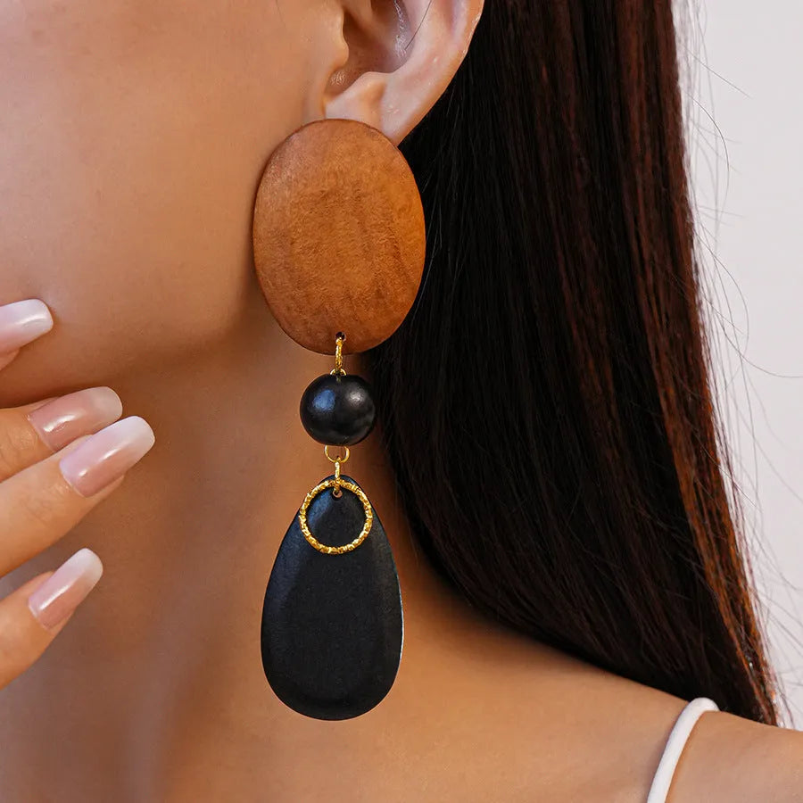 Pair of brown-black retro wooden ellipse earrings for women on a plain background.