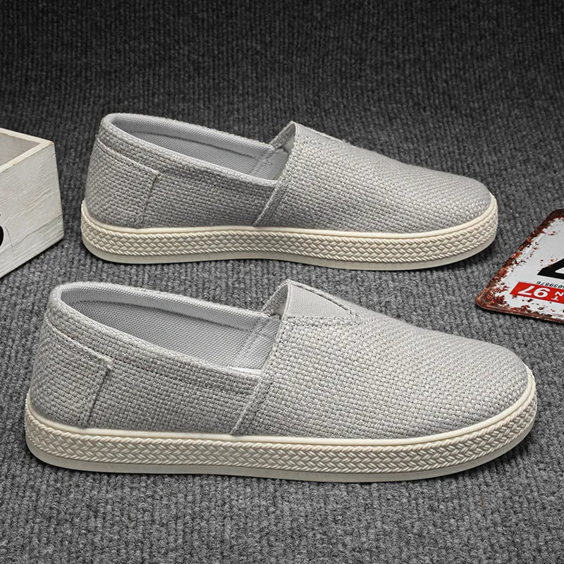 Men's beige linen canvas slip-on shoes with round toe and shallow cut design on a grey background.