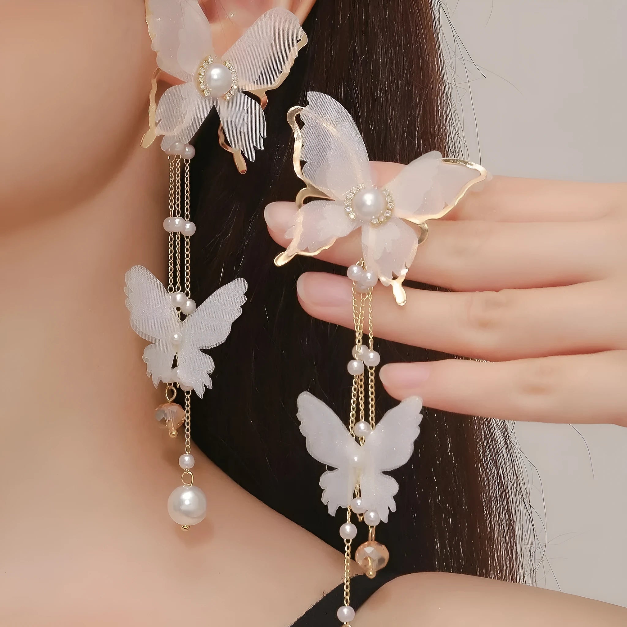 Close-up of white butterfly-shaped earrings with pearl and rhinestone details, featuring a dangling tassel on a model's ear.