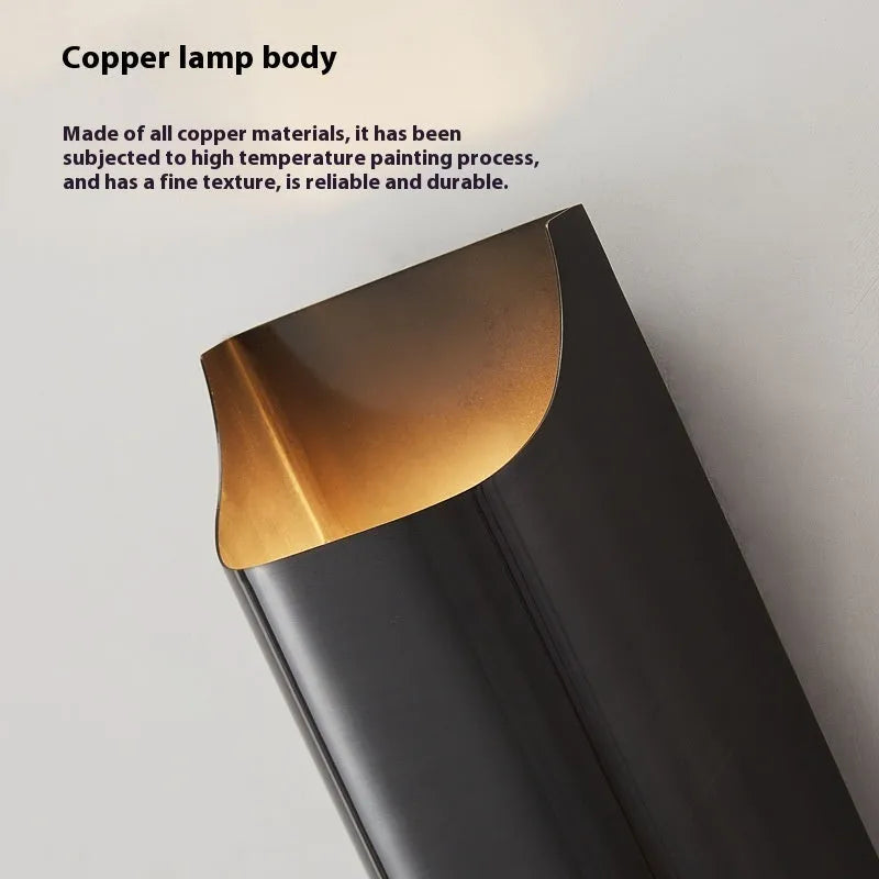 Minimalist copper wall lamp in black gold finish mounted beside a bed.