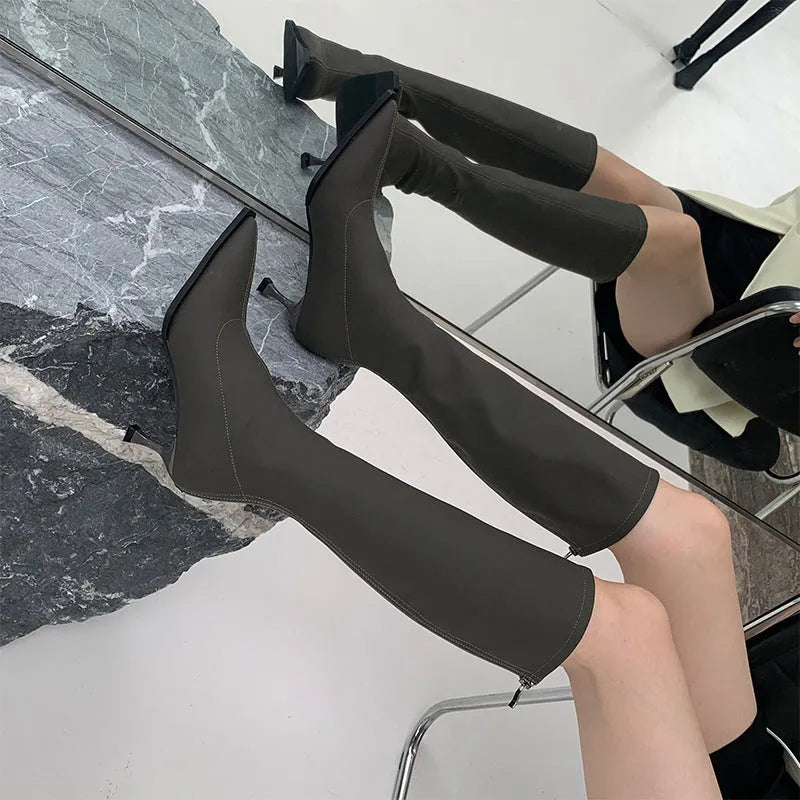 Women's black pointed toe below-knee boots with a stiletto heel and a back zipper on a plain background.