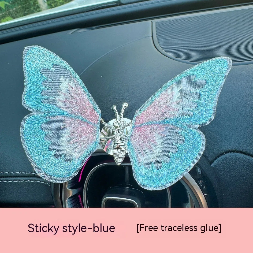Soft fabric embroidered butterfly car air vent decoration in multiple colour options on a centre console.